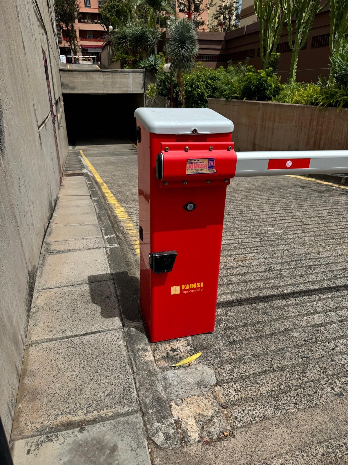 Puerta de estacionamiento roja con parte superior blanca, brazo levantado, al lado de una entrada a un estacionamiento subterráneo.