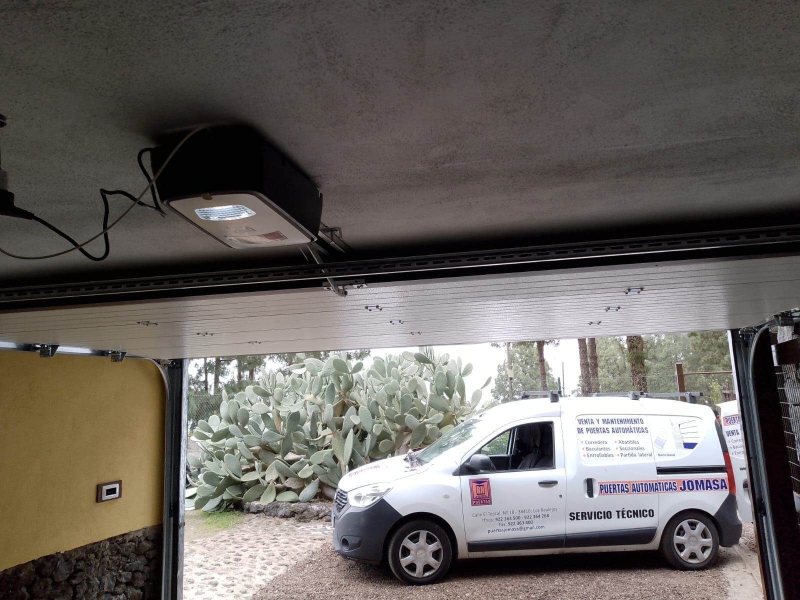 Interior de garaje con una puerta abierta que revela una furgoneta de servicio blanca estacionada afuera.