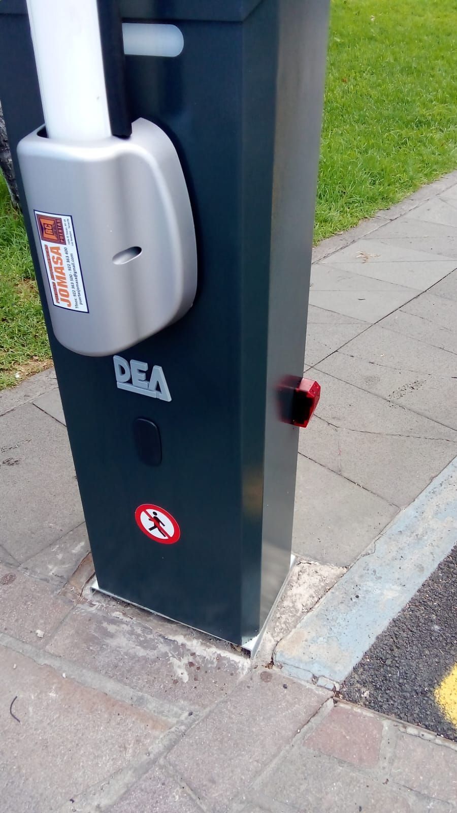 Puerta de estacionamiento gris oscuro con botón de parada rojo, brazo blanco y señal de seguridad, montada en la acera.