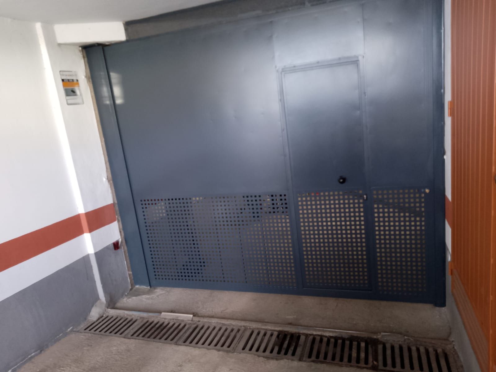 Puerta de garaje de color azul oscuro con puerta pequeña, sobre rejilla.