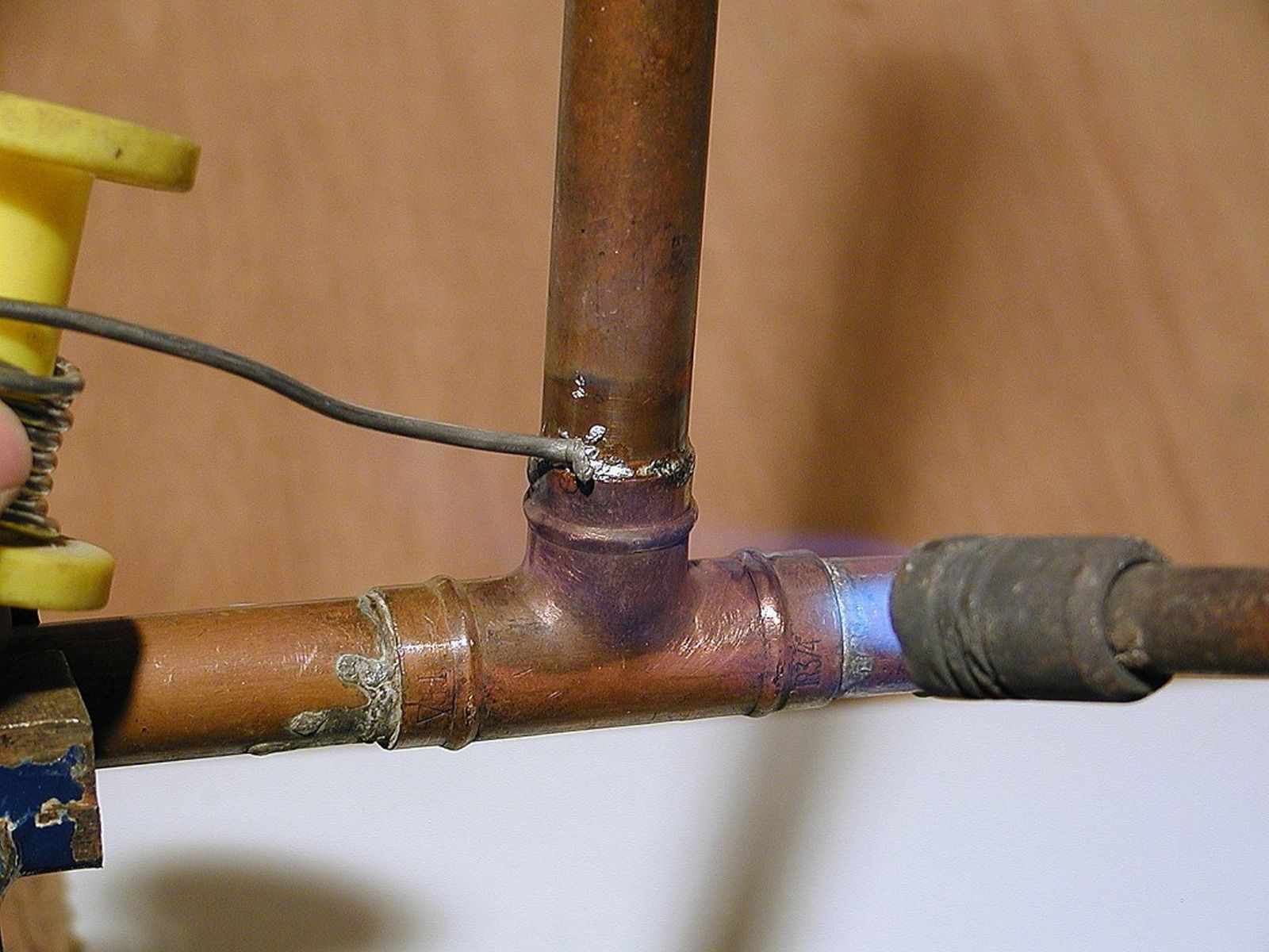 Soldering copper pipes with a flame torch and wire, indoors.