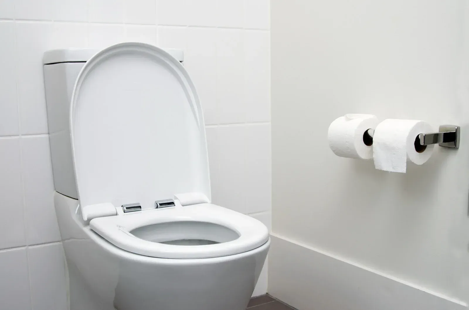 White toilet with the lid open, beside a wall-mounted toilet paper holder with two rolls.
