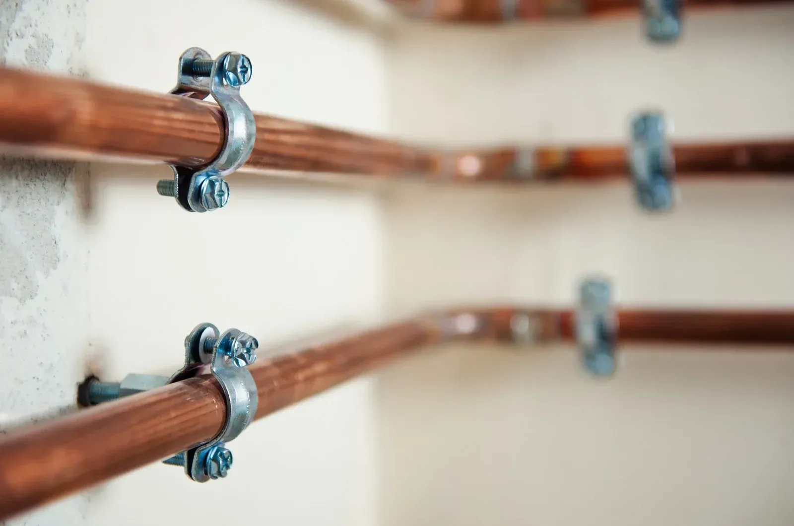 Copper pipes secured to a white wall with metal clamps.