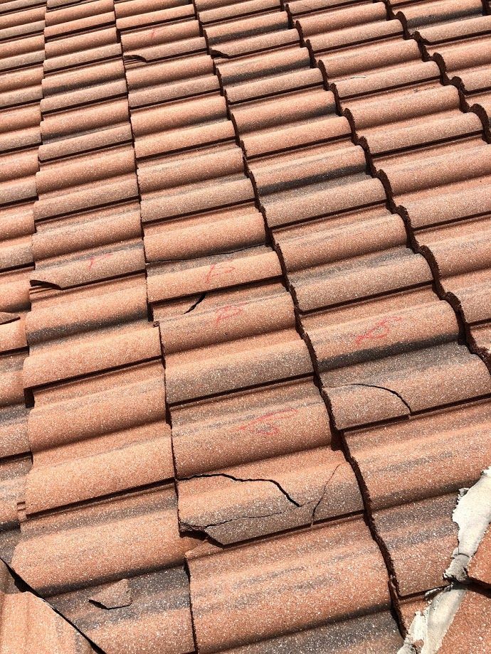 A section of a terracotta-colored tiled roof showing several cracked and broken tiles.