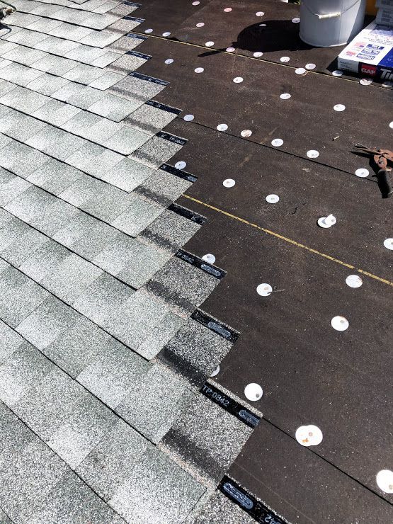 Partial installation of grey asphalt shingles on a roof over black felt underlayment secured with white plastic caps.