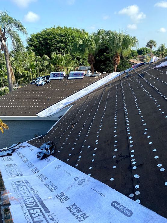 A roof under construction covered in black underlayment with rows of fasteners and white protective film strips.