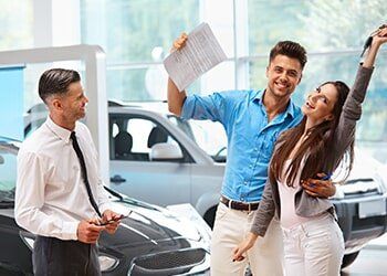 Young Couple Celebrating the Purchase of a Car in a Showroom — Friendly Finance in Central City, KY