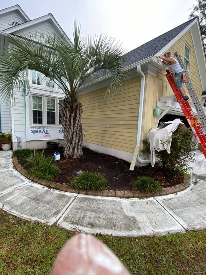 A man is painting the side of a house with a ladder.