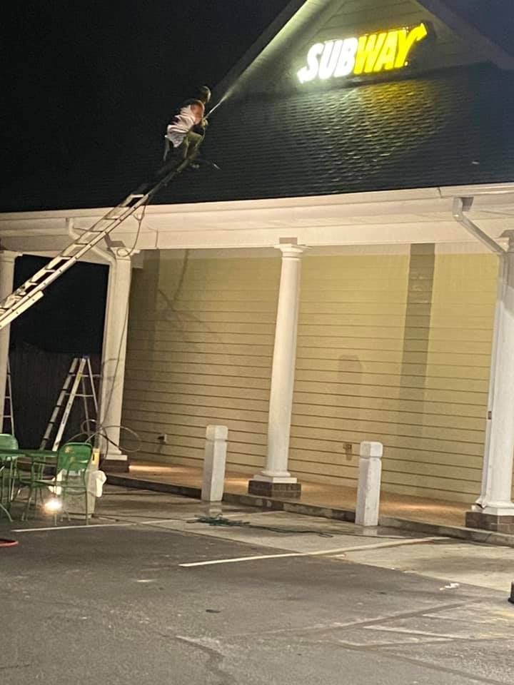 A man is cleaning the roof of a subway restaurant at night.