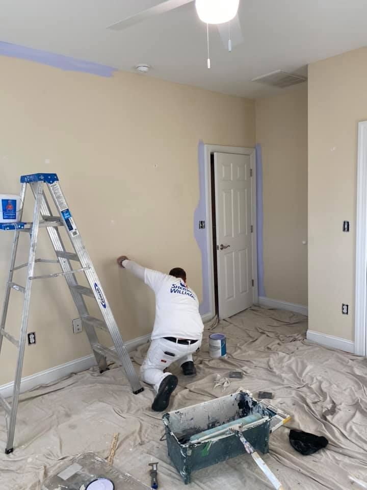 A man is painting a wall in a room with a ladder.