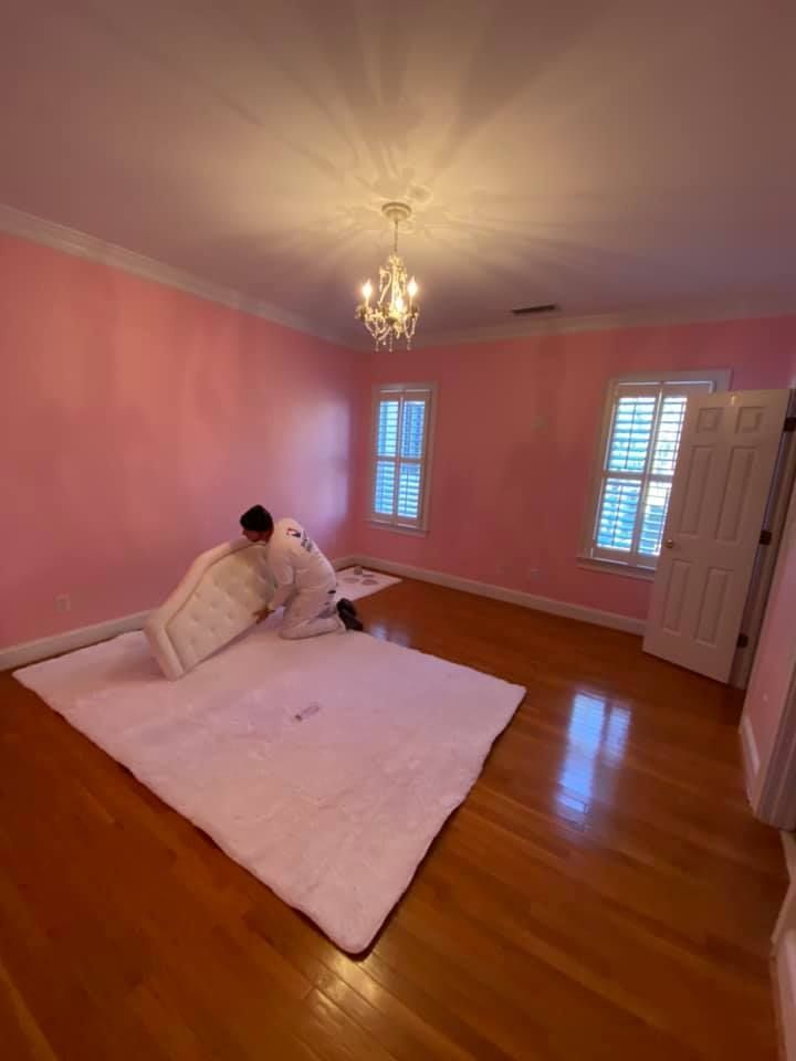 A person is laying on a white rug in a room with pink walls.