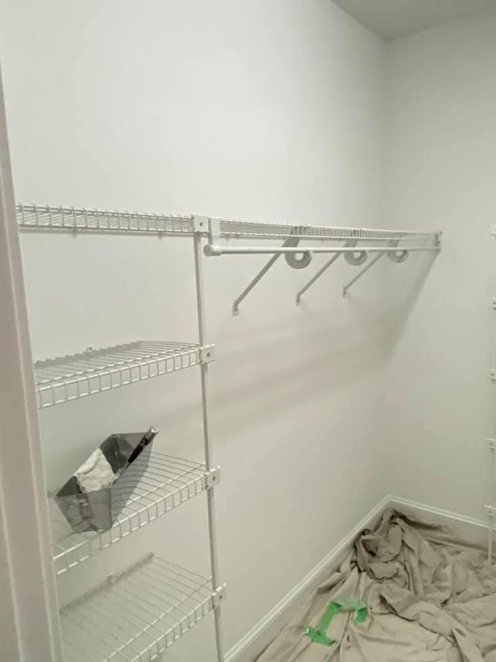 A walk in closet with white shelves and clothes racks.