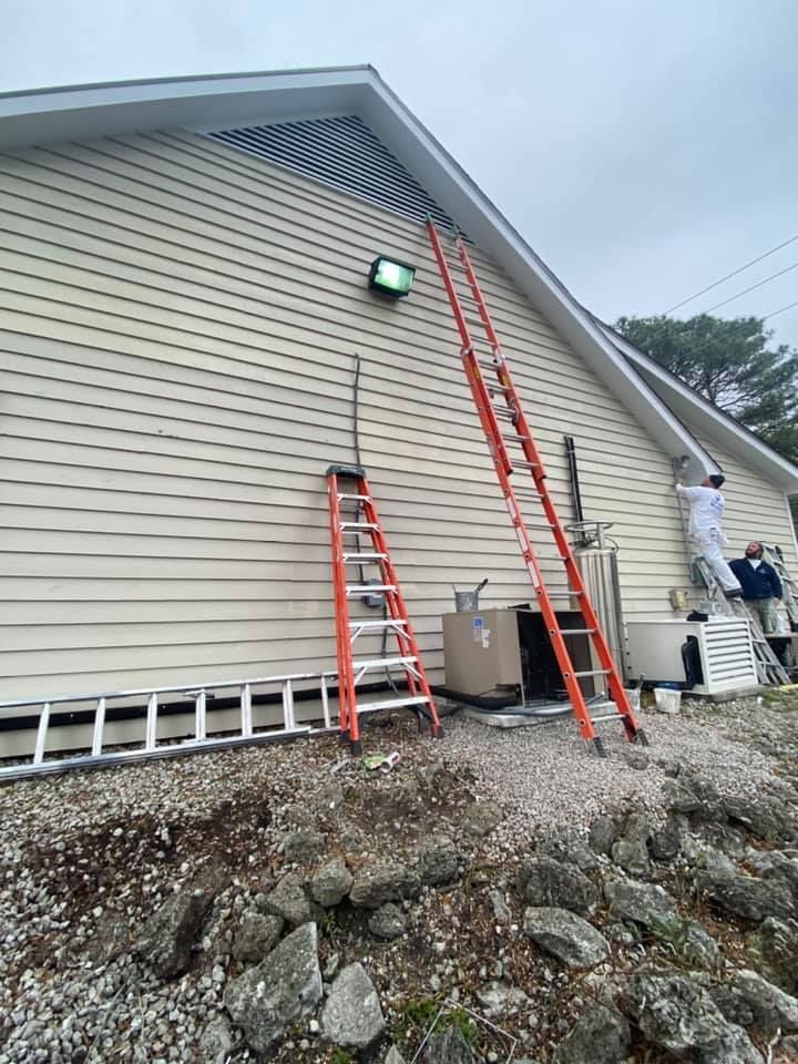 A man is painting the side of a house with a ladder.