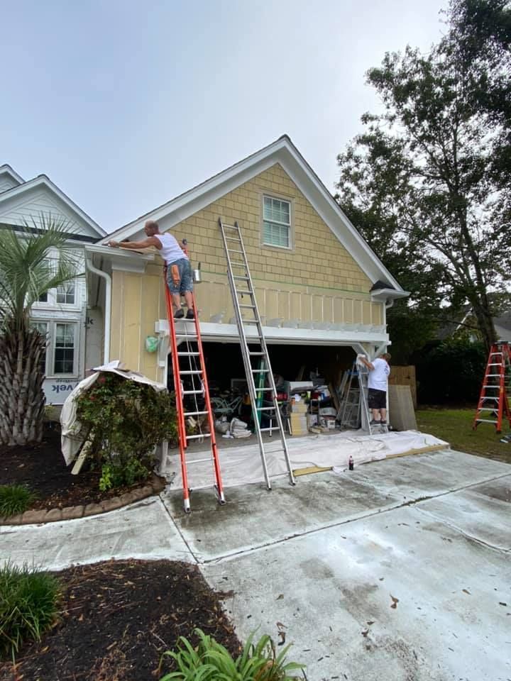 A man is standing on a ladder painting the side of a house.