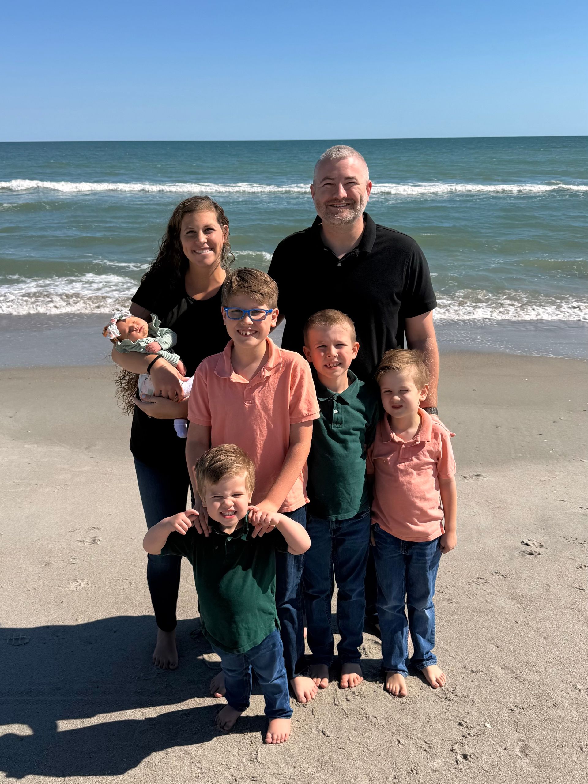 Family of five standing on a beach with waves in the background, smiling at the camera.