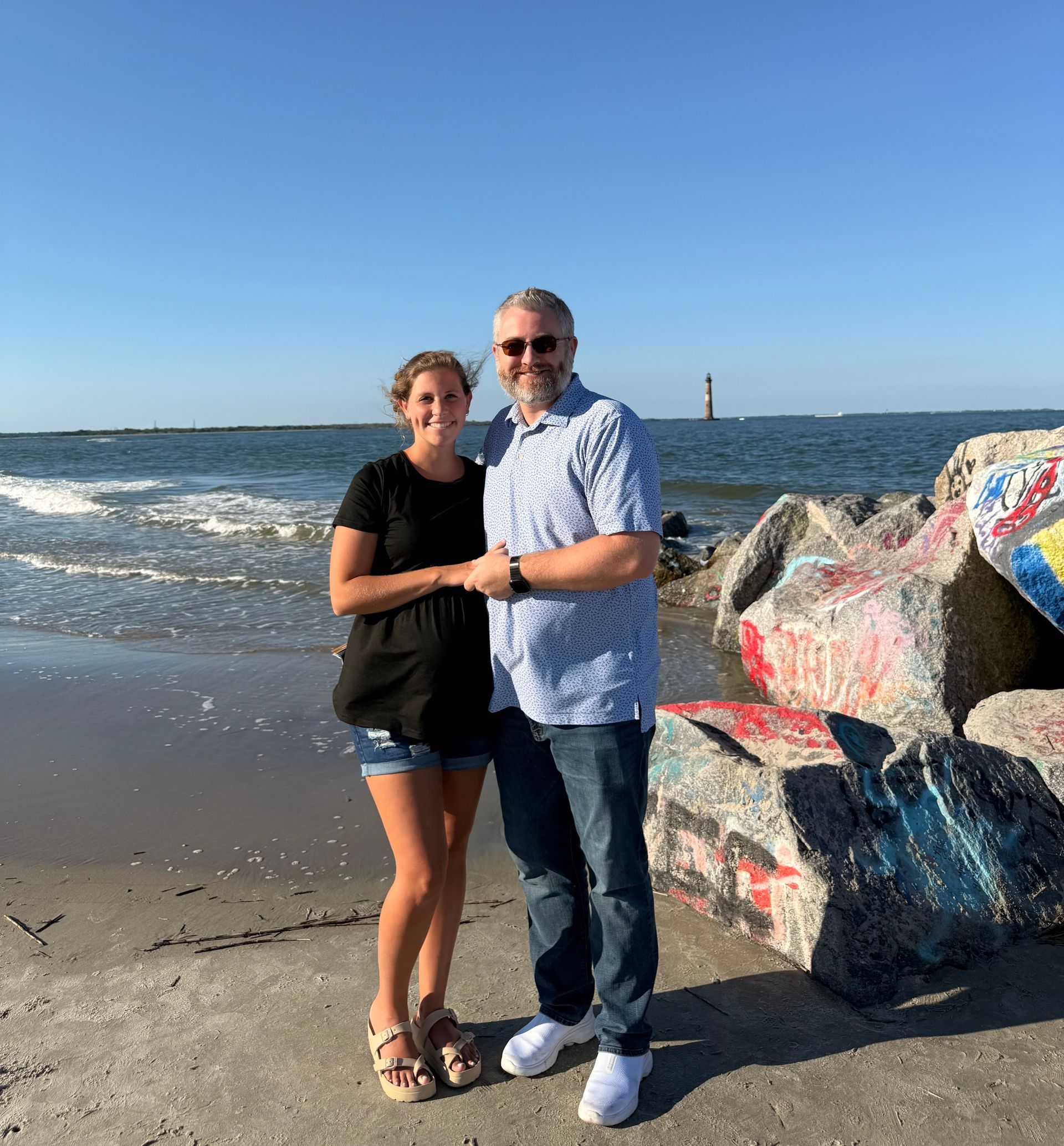 Two people standing on a beach beside painted rocks with waves and blue sky in the background