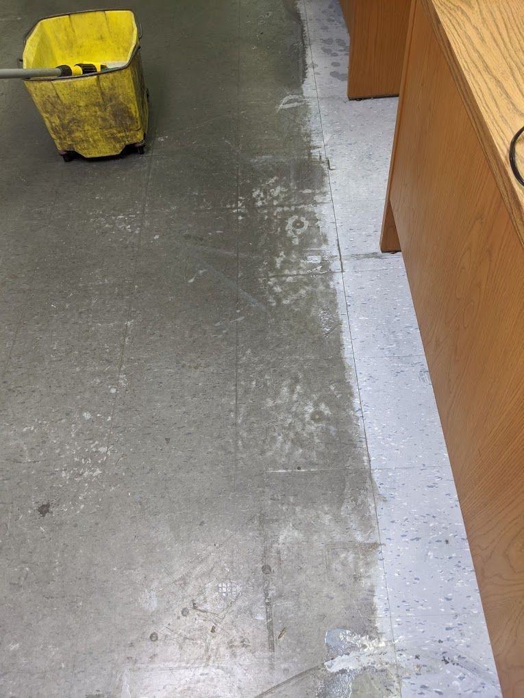 A yellow mop is sitting on a dirty floor next to a desk.