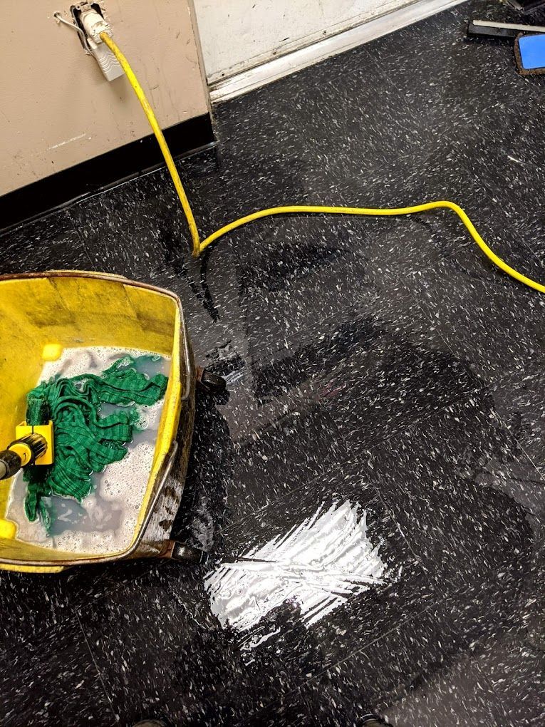 A mop is sitting on the floor next to a yellow hose.