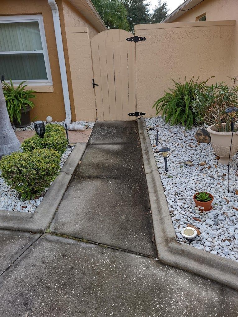 A concrete walkway leading to a house with a wooden gate.
