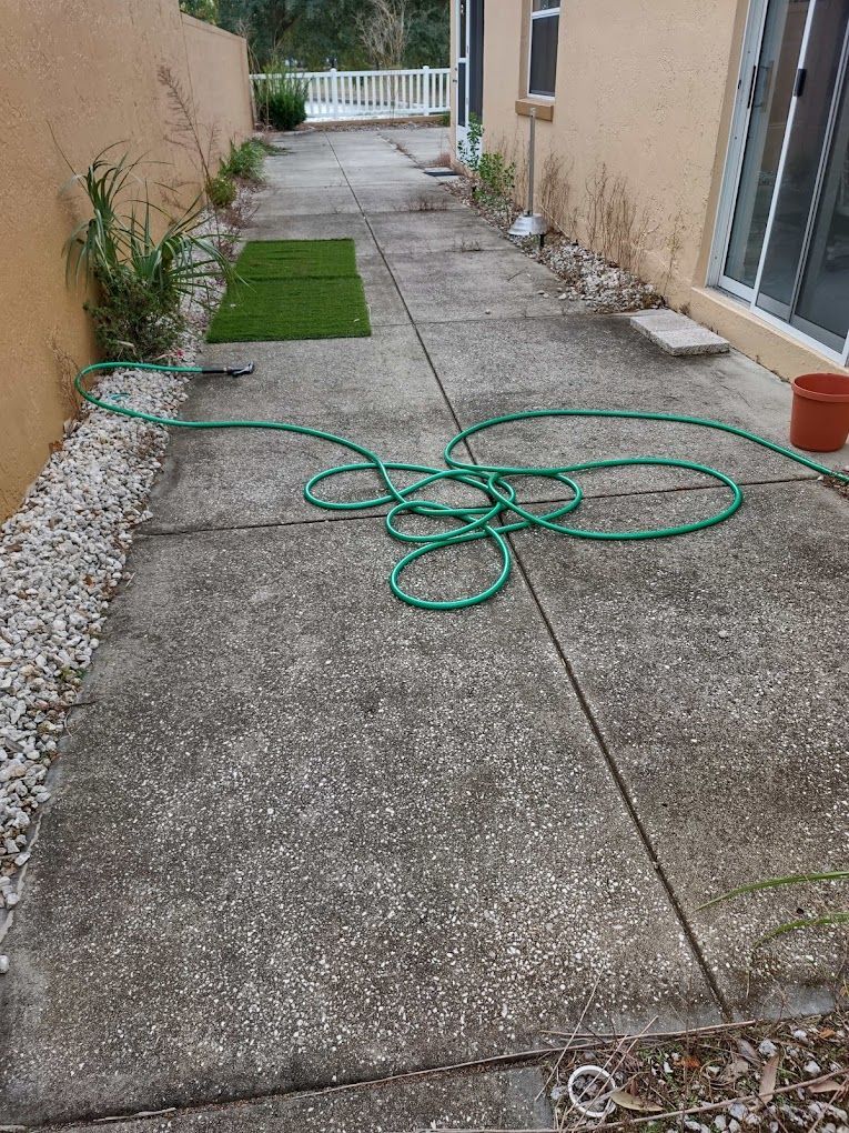 A green hose is laying on a concrete sidewalk next to a house.