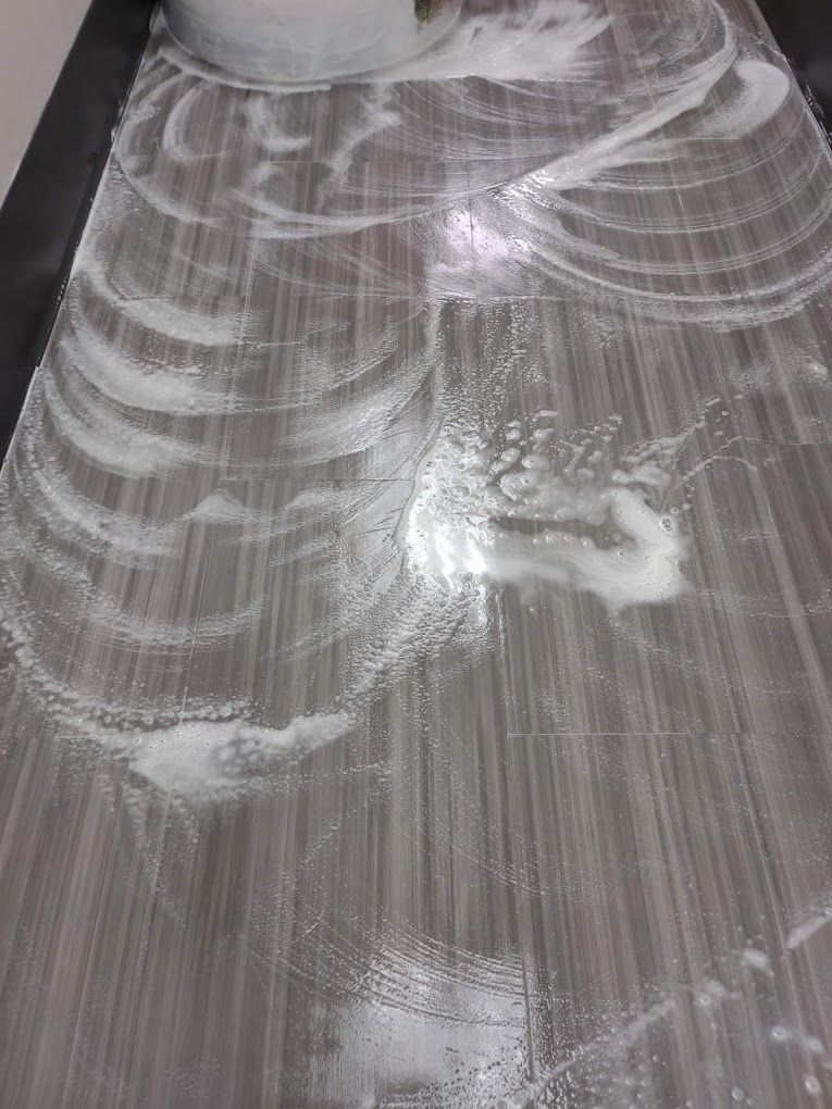 A person is cleaning a tiled floor with soap and water.