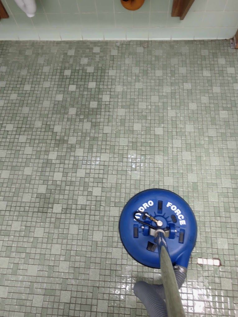 A person is cleaning a tiled floor with a vacuum cleaner.