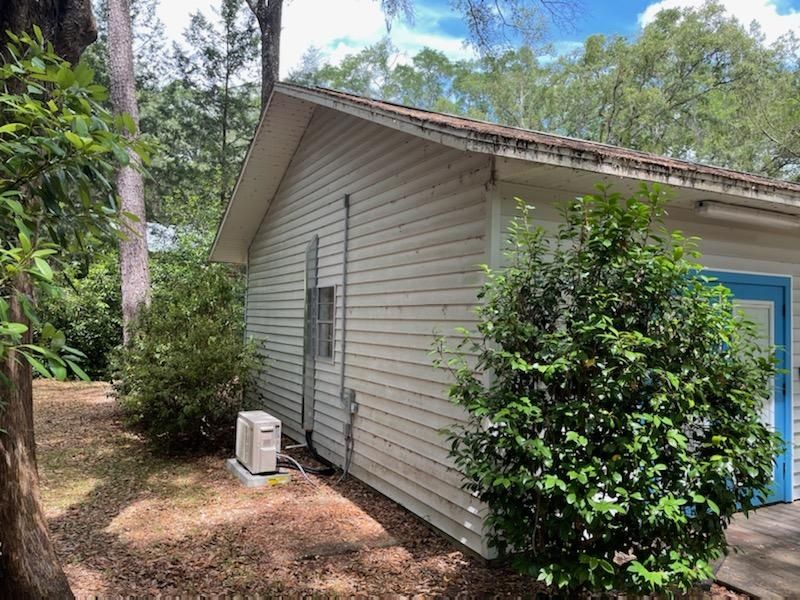 A white house with a blue door is surrounded by trees and bushes.