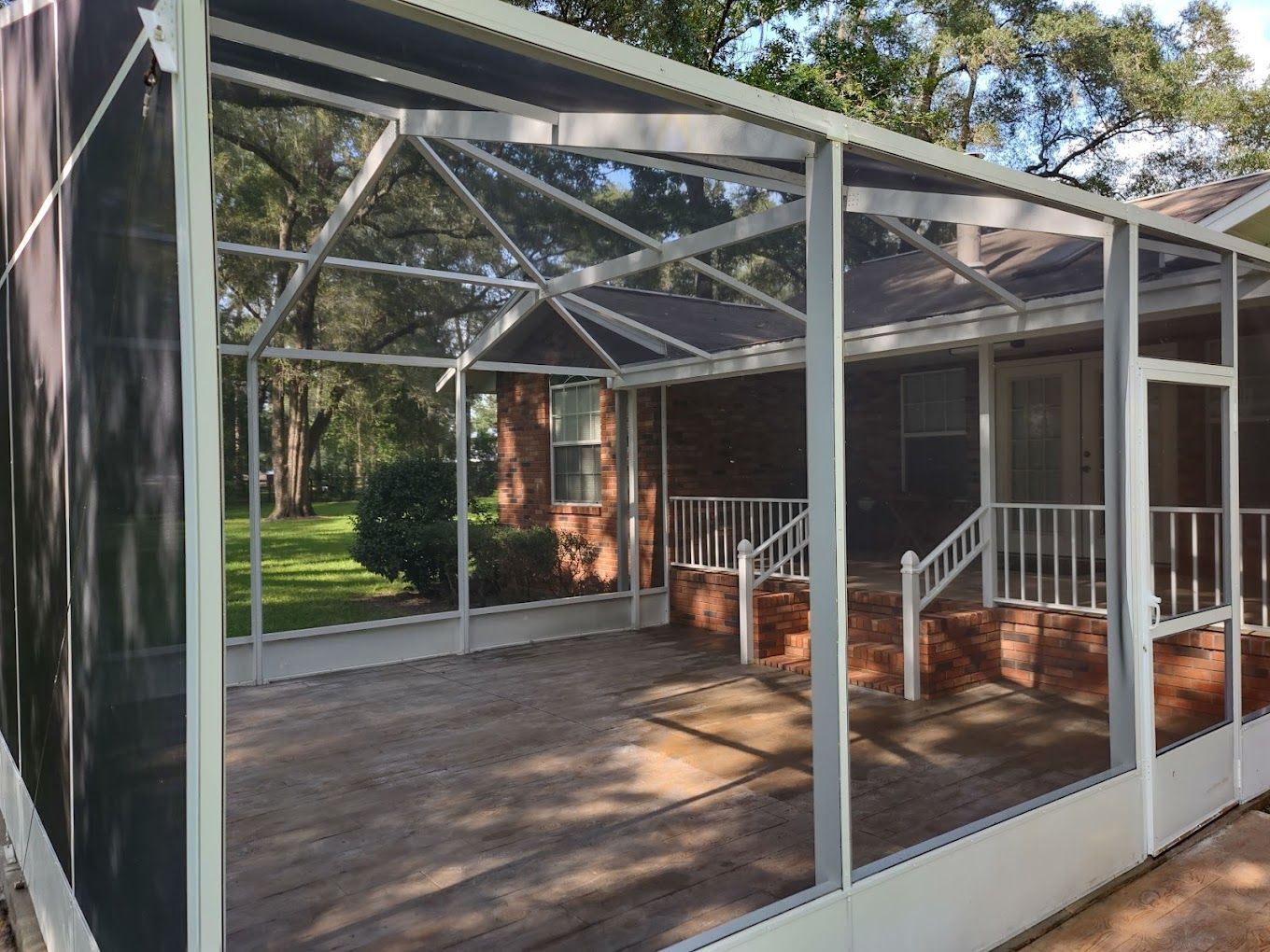 A screened in porch with a brick house in the background.
