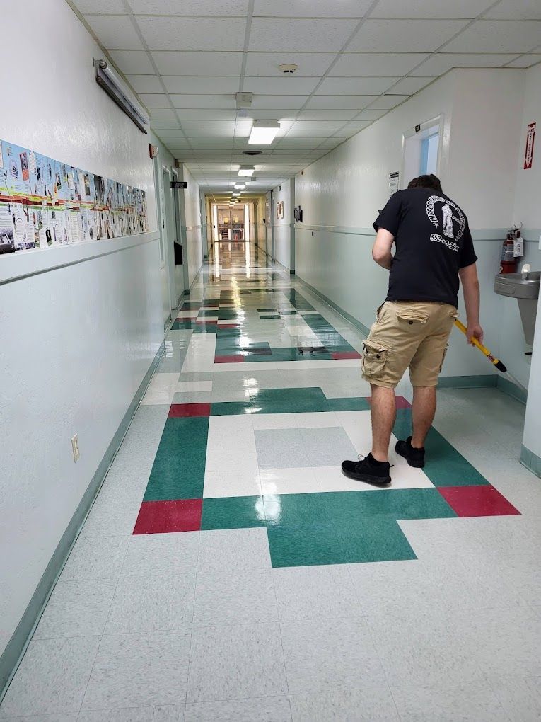 A man in a black shirt is sweeping the floor of a hallway