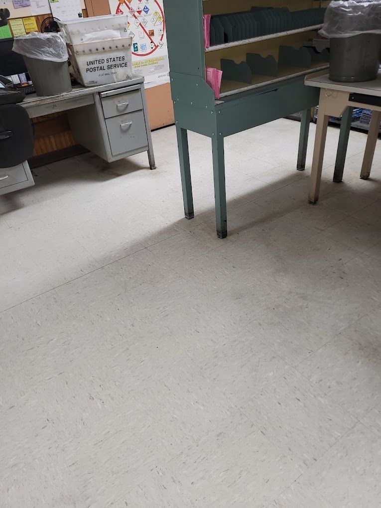 A classroom with a desk , chairs , and a trash can.