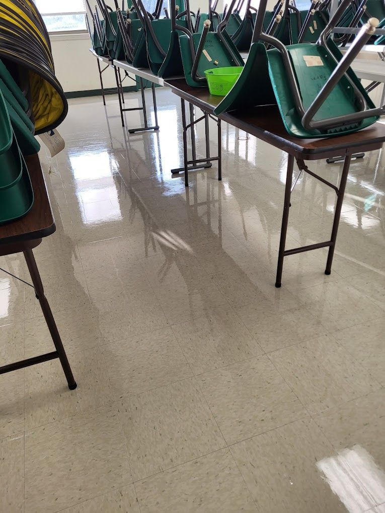 A row of folding tables with green chairs on them in a classroom.