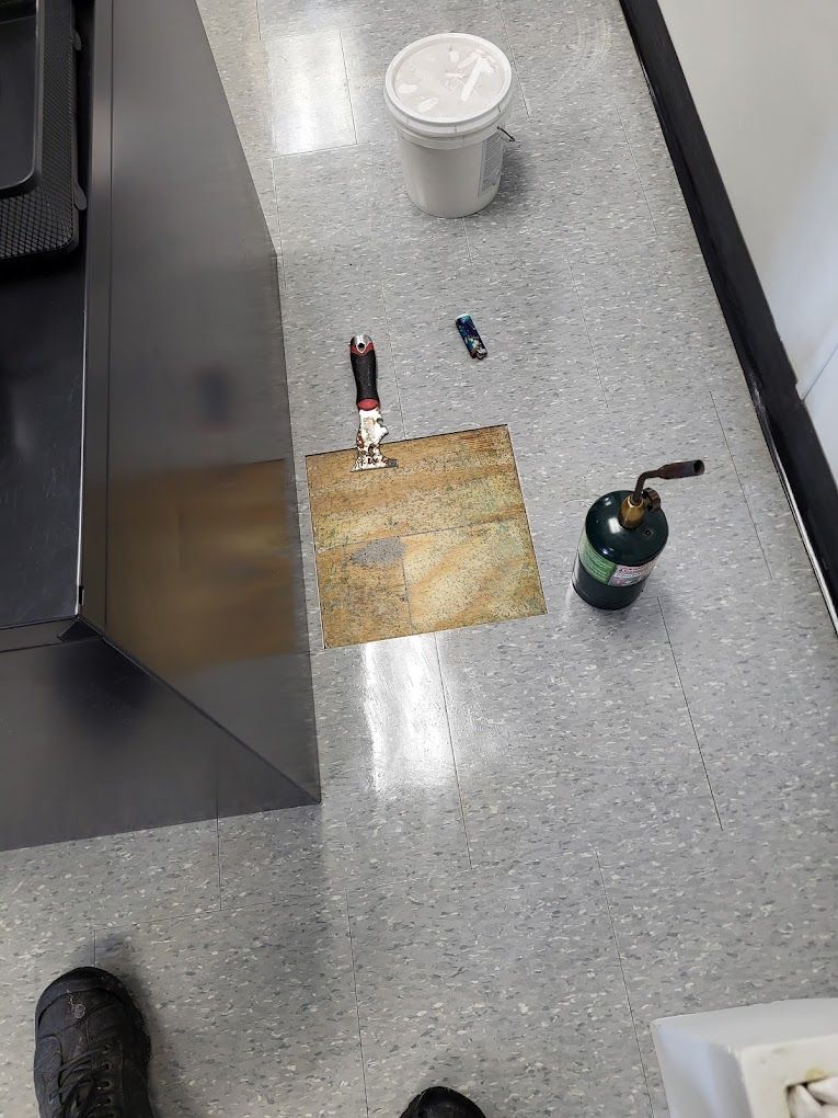 A person is standing on a tiled floor next to a bucket and a bottle of gas.