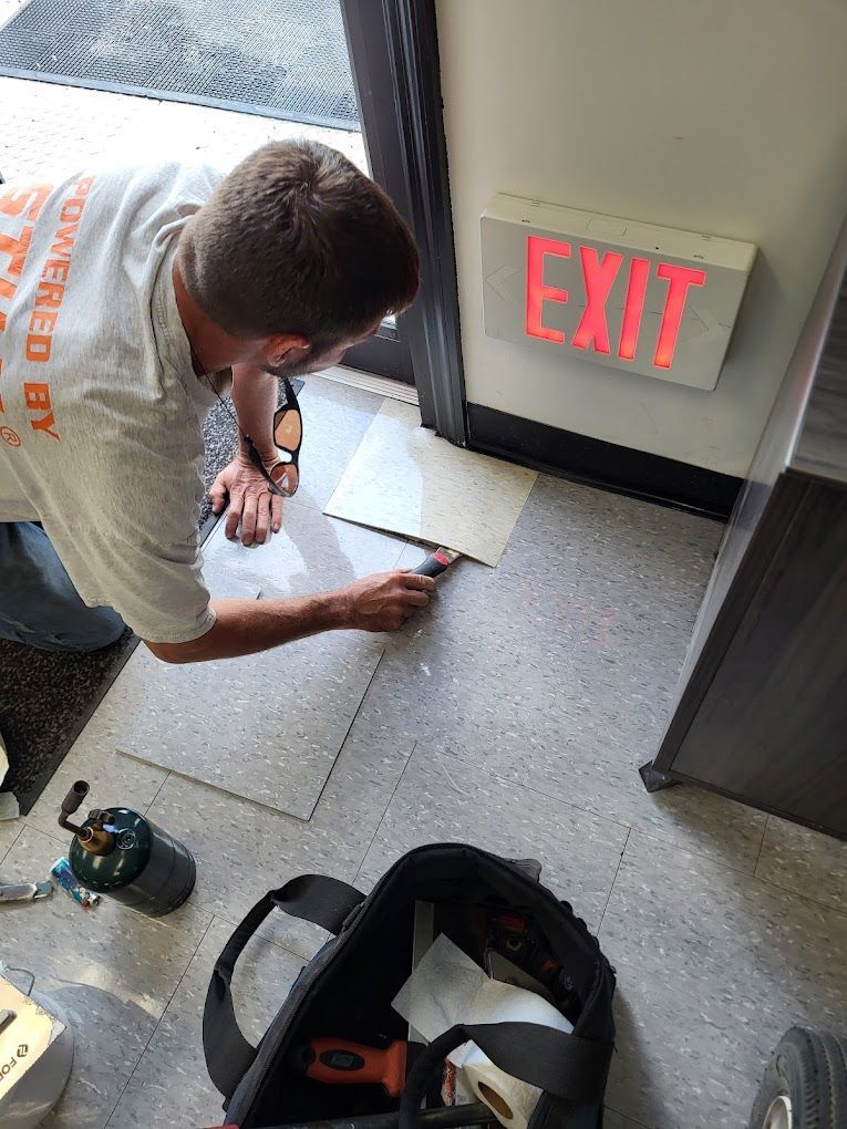 A man is working on a tile floor next to an exit sign.