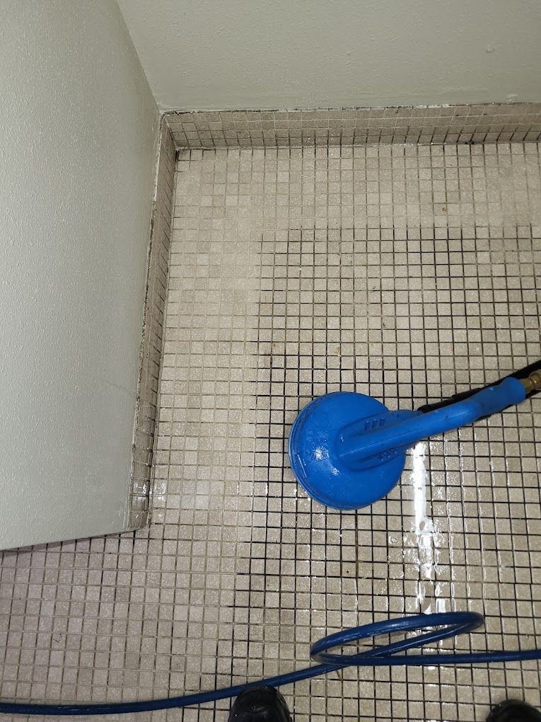 A blue shower head is sitting on a tiled floor next to a blue hose.