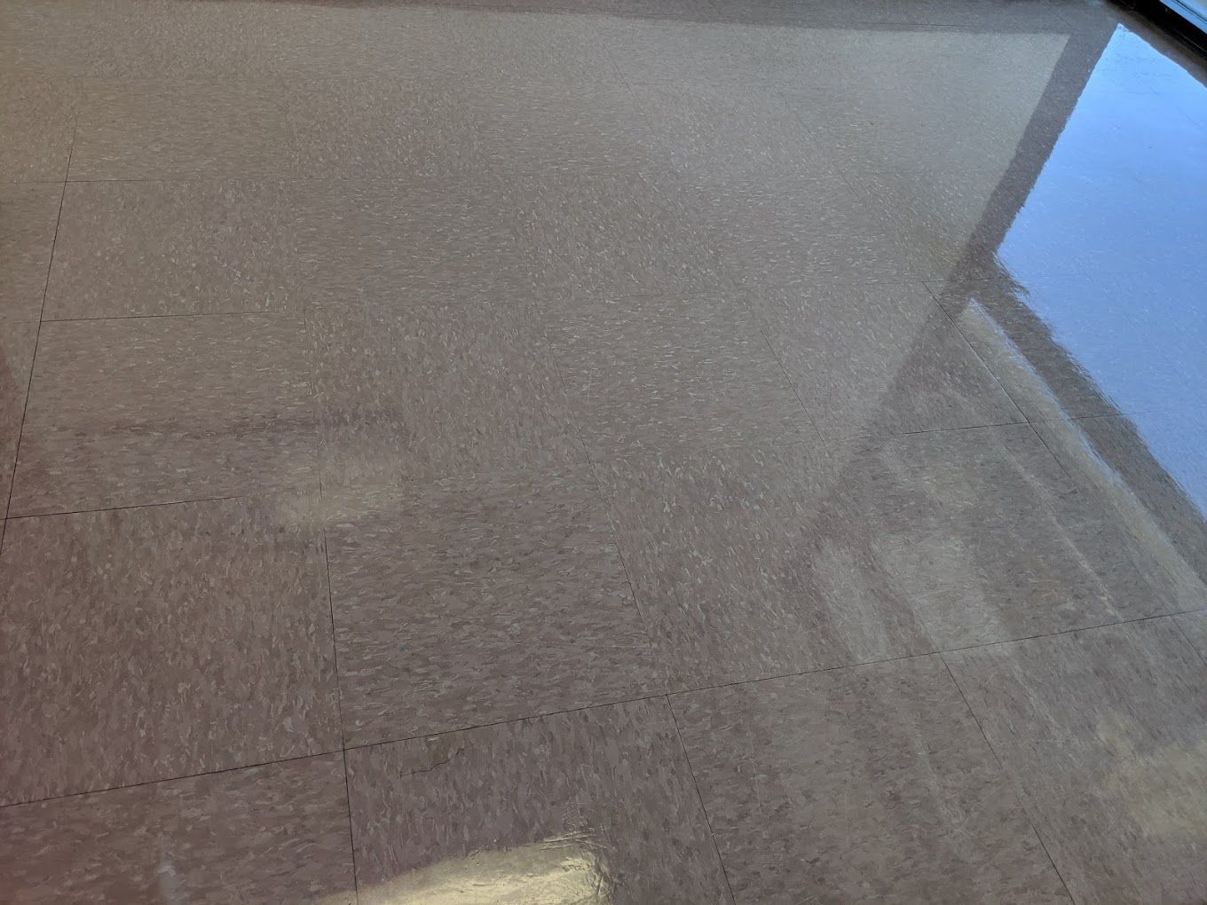 A close up of a tiled floor with a window reflected in it.
