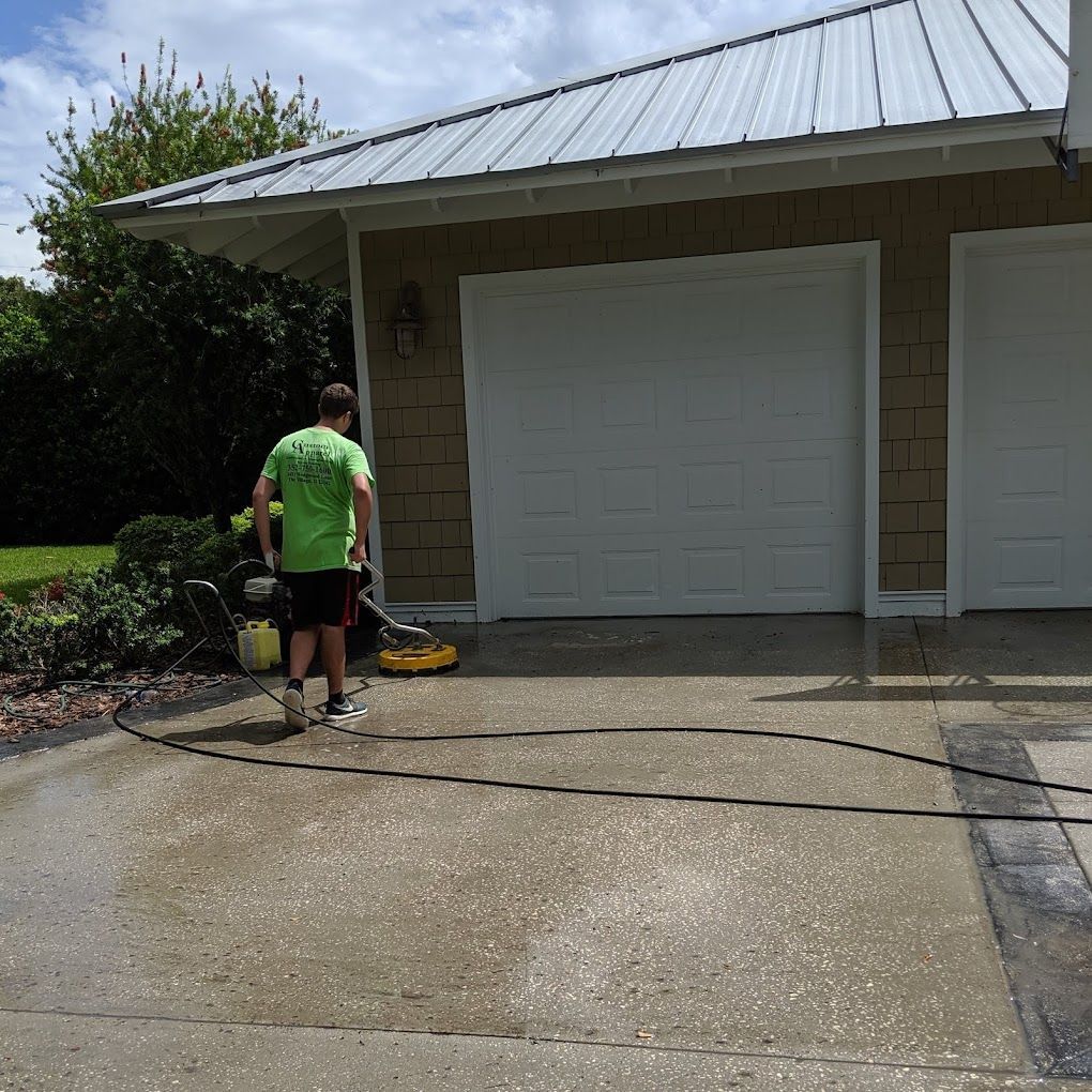 A man in a green shirt is cleaning a driveway in front of a garage.