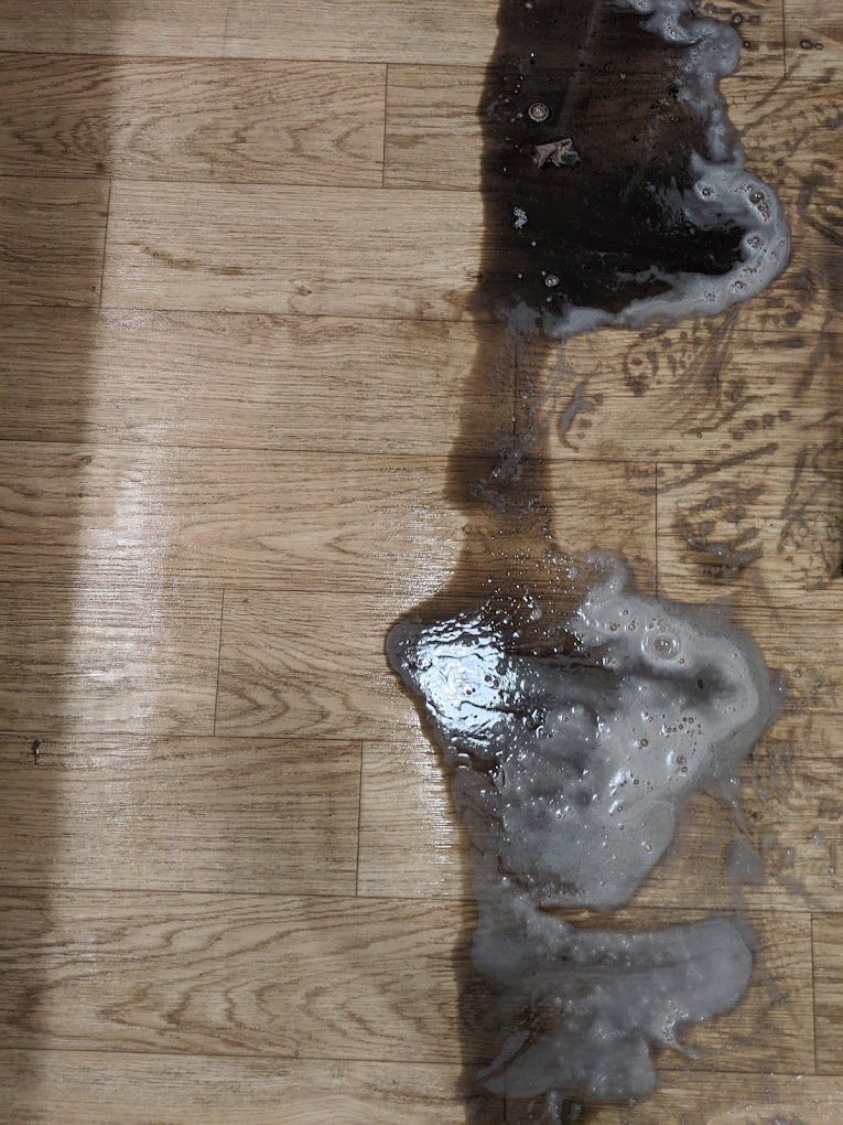 A close up of a puddle of water on a wooden floor.