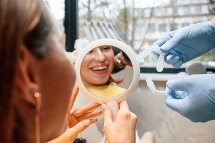 Woman smiling in mirror at dentist | Best cosmetic dentist in Pleasant Hill CA | Veneers, Whitening, Crowns