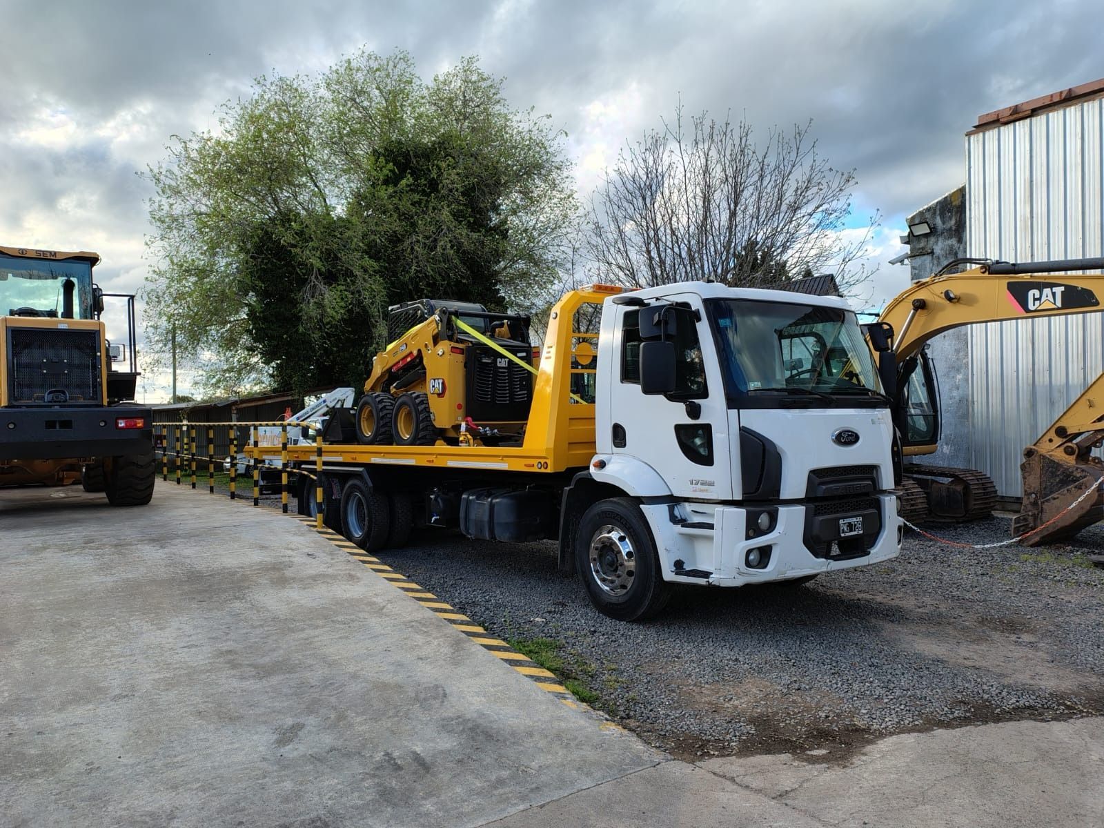 Camión de remolque blanco que transporta equipo de construcción amarillo sobre una superficie de hormigón.