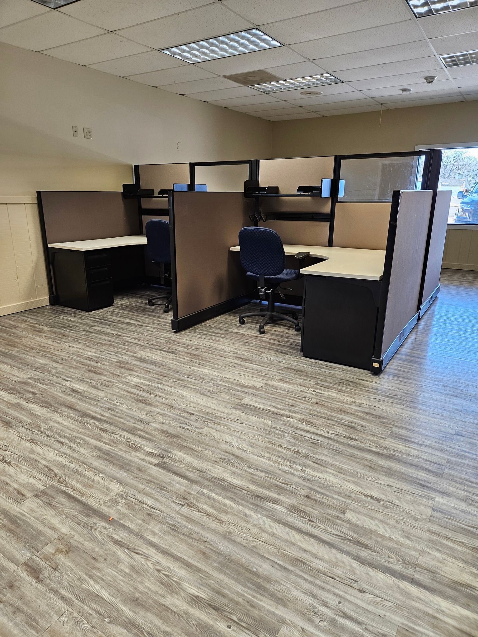 Office cubicles with dark desks and tan dividers in a room with linoleum flooring.