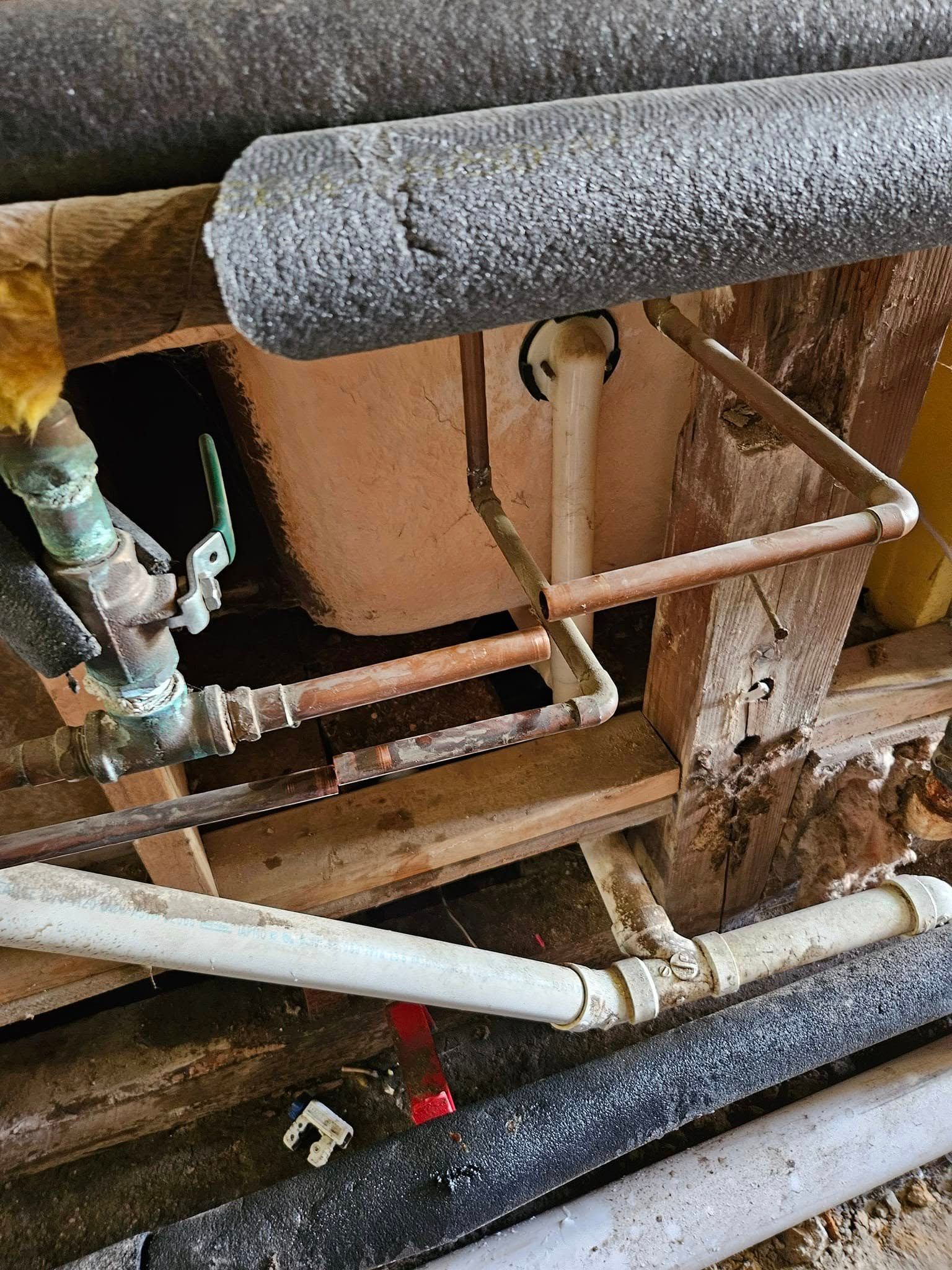 Plumbing pipes under a bathtub with copper piping and insulation, showing parts of the drain and fittings.