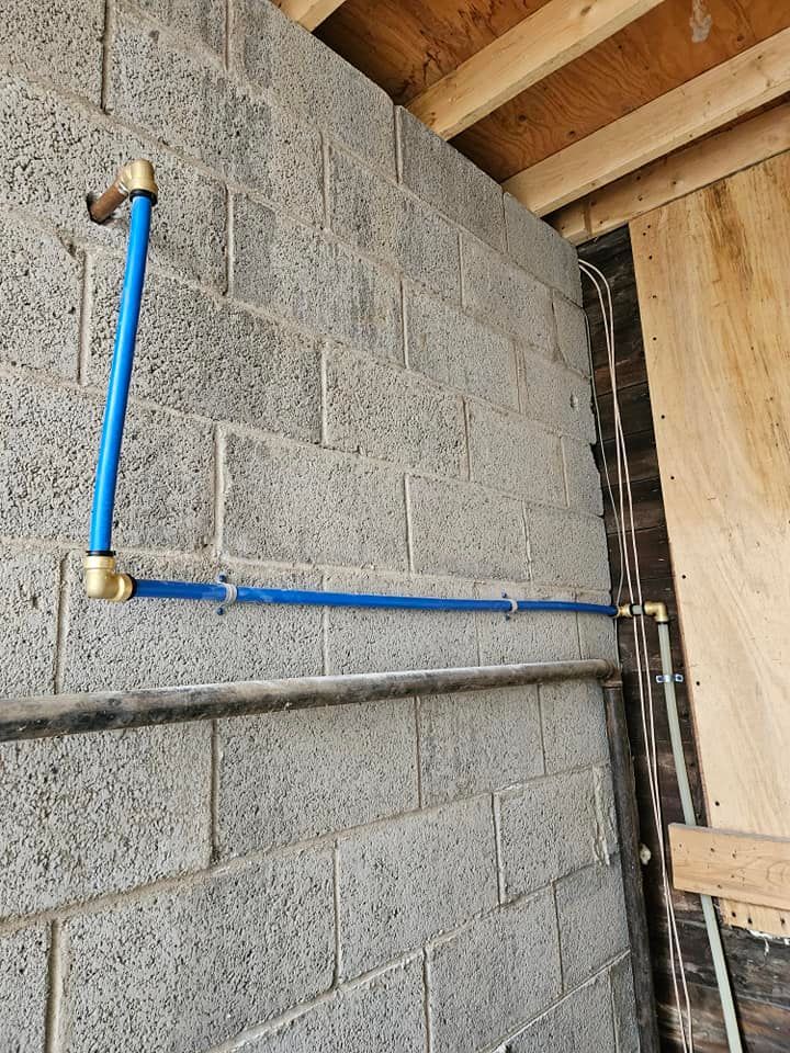 Blue water pipes, with brass fittings, run along a concrete block wall.