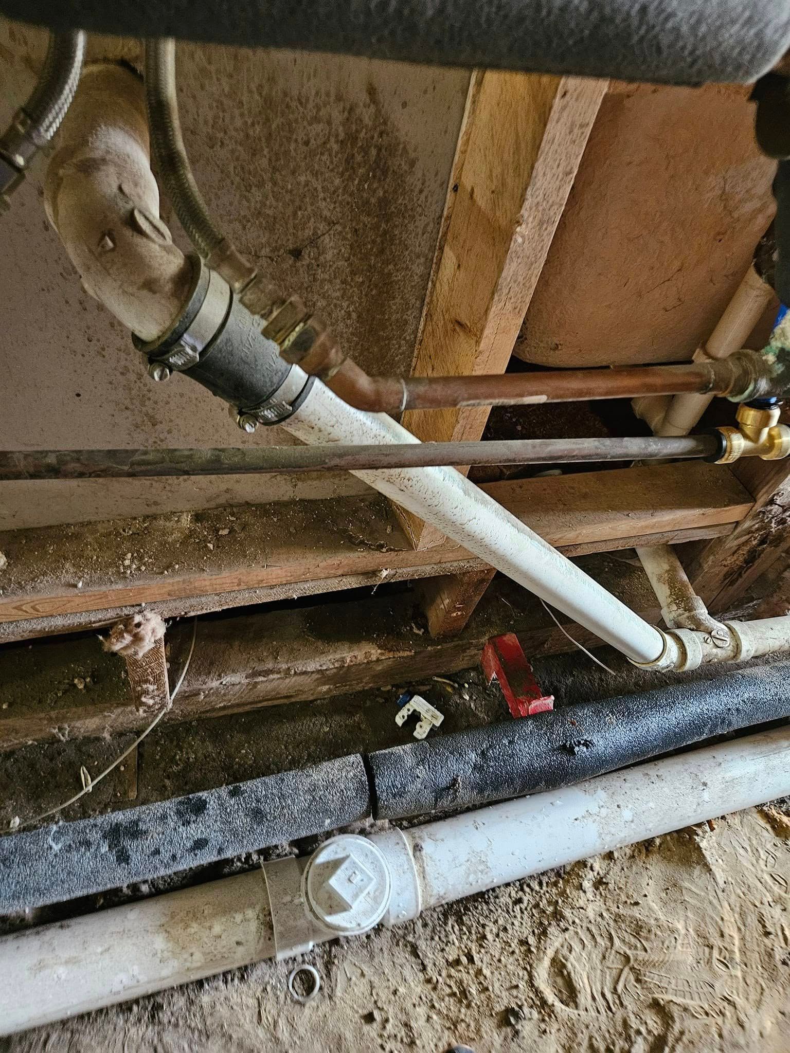 Plumbing pipes, white and black, against a wooden structure. Some pipes are connected with rubber.