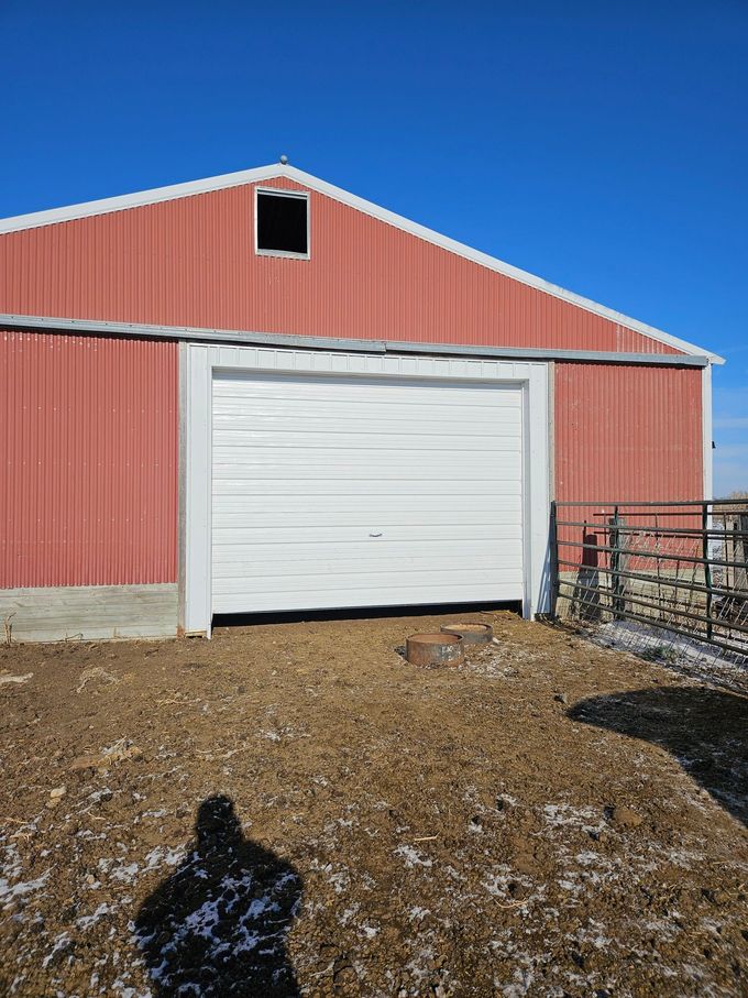 Red barn with a white garage door on a sunny day. Shadow of person in the foreground.