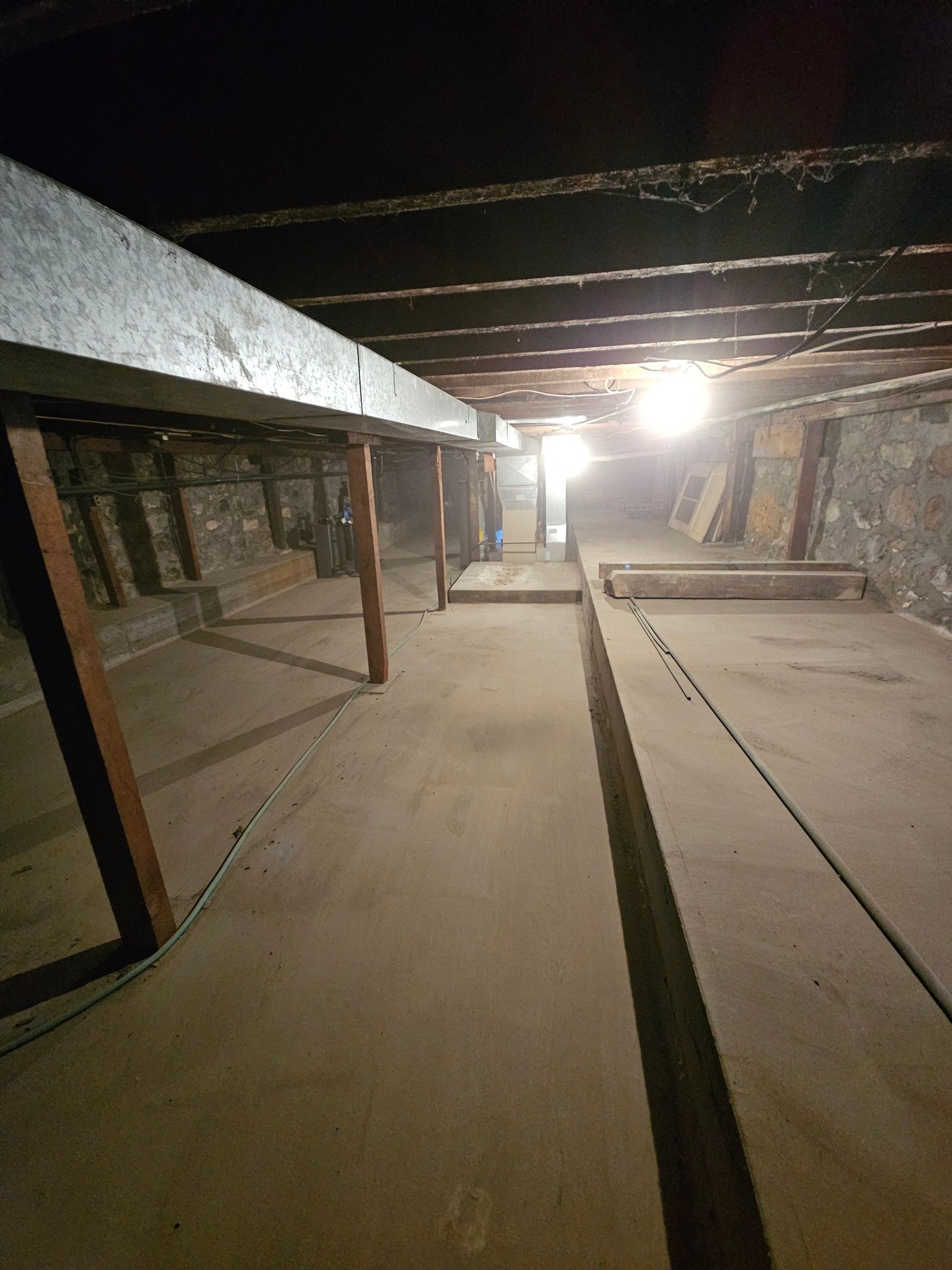 A dark, unfinished basement with concrete floor, exposed beams, and support posts.