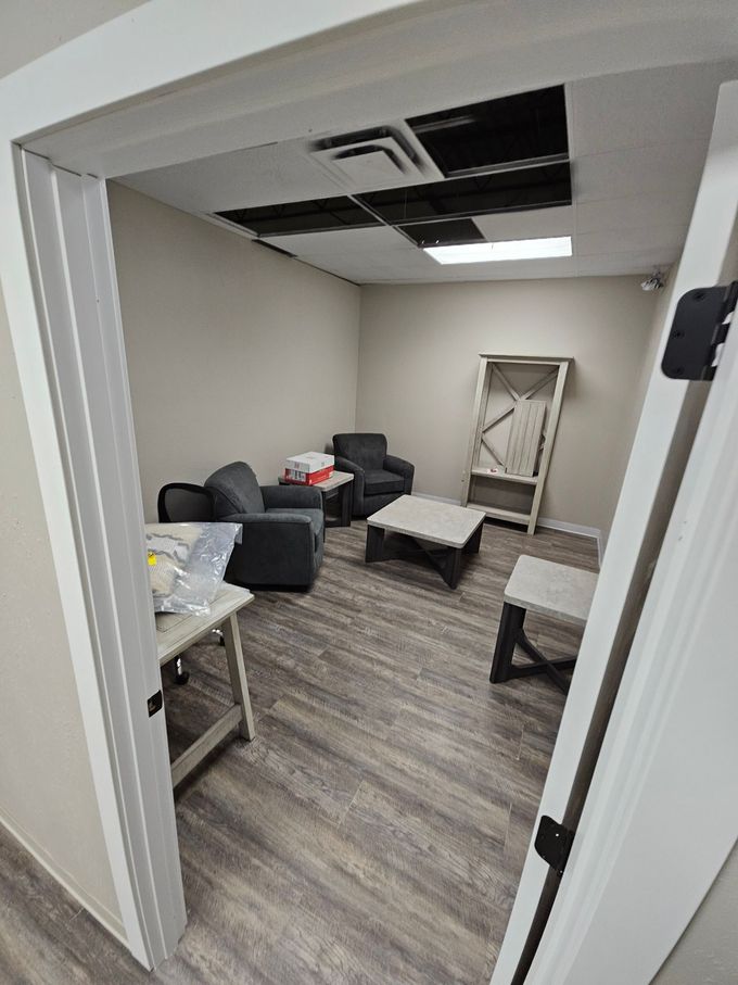 Room interior with seating, a table, and open ceiling panels. Gray and white tones dominate the space.