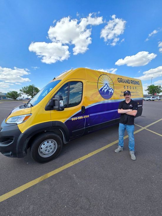 Man in front of a yellow/purple van with company logo in a parking lot, arms crossed.