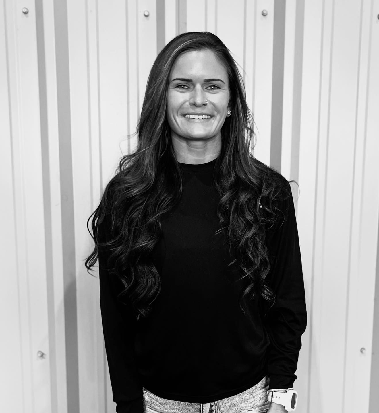A woman with long hair is smiling in a black and white photo.
