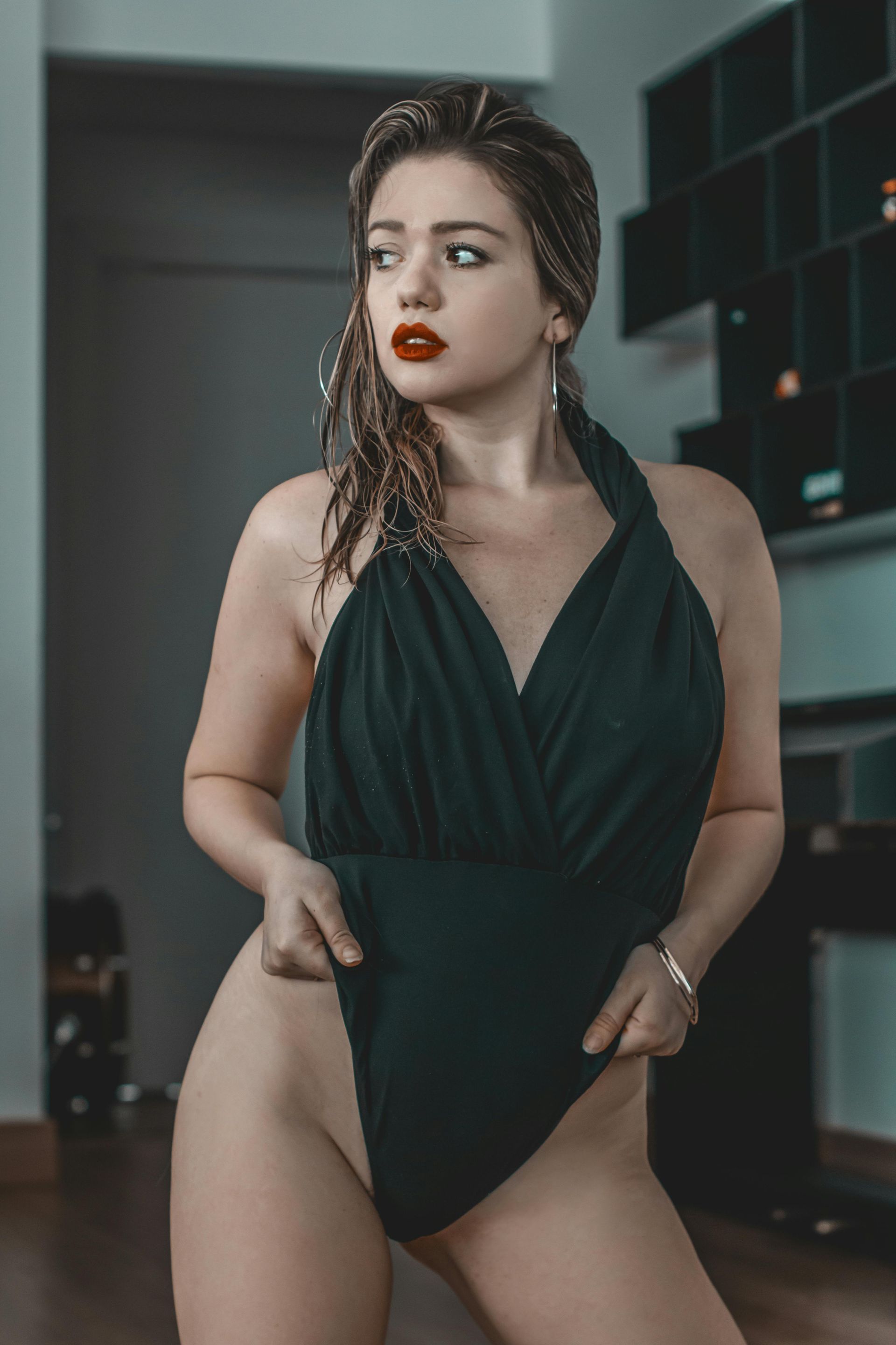 Woman in a black halter bodysuit, holding the fabric at her hips. She has red lipstick