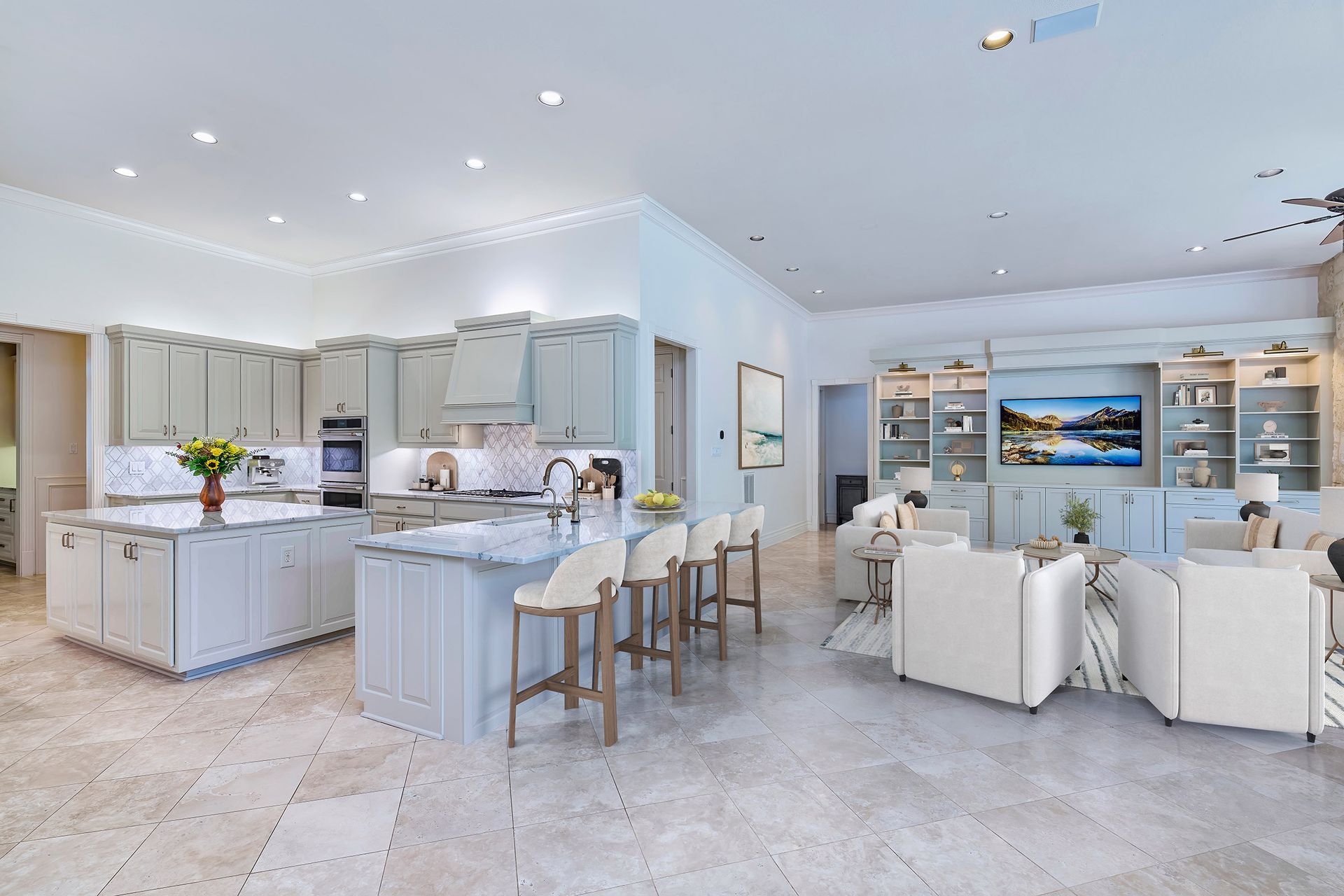 Bright open-plan kitchen and living room with white cabinets, island seating, and sofas around a TV.